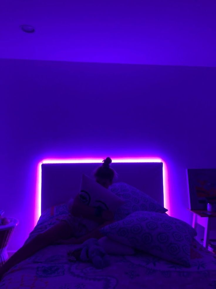 a person laying in bed under a purple light with their head on the pillow,