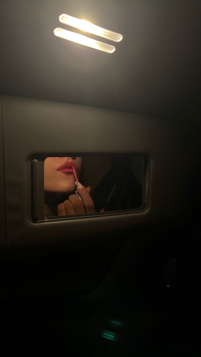 a woman's reflection in the side mirror of a car at night with lights on