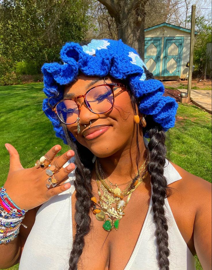 a woman with blue hair and glasses making the peace sign while standing in front of some grass