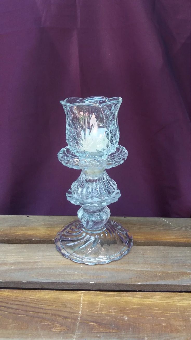 a clear glass candle holder sitting on top of a wooden table next to a purple wall