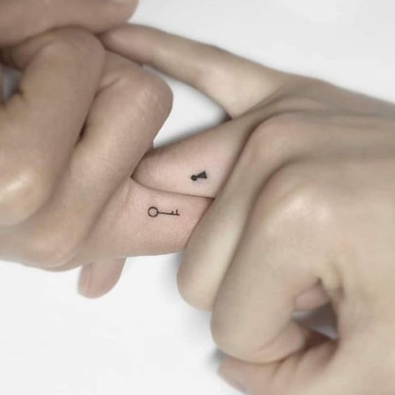 two hands holding each other with small tattoos on their thumbnails and one has an arrow in the middle