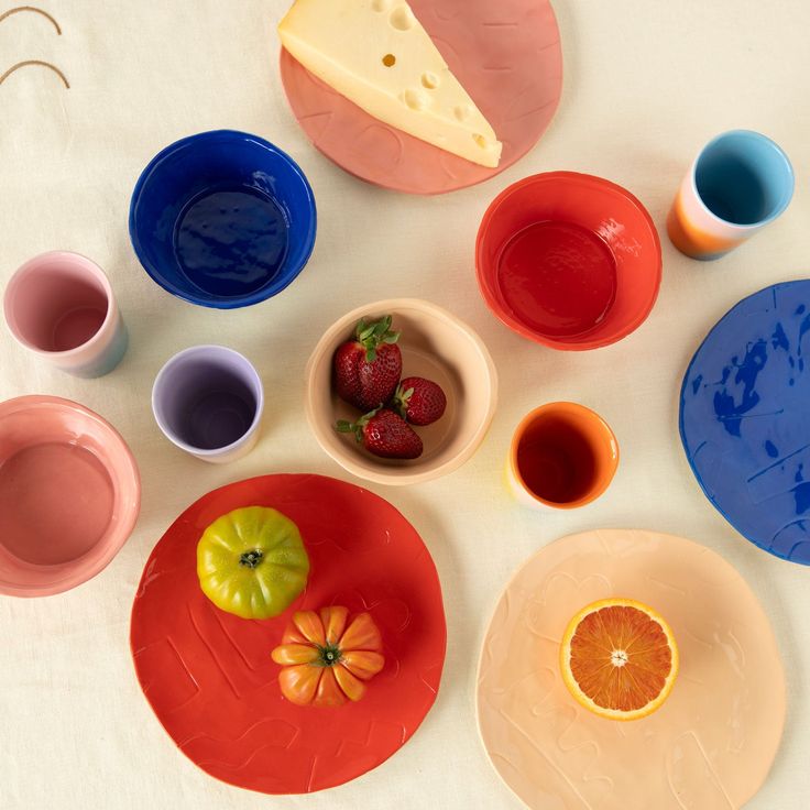 colorful plates with fruit and cheese on them sitting on a white tableclothed surface