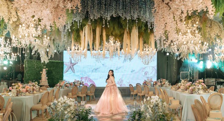 a woman standing in front of a stage with flowers and chandeliers