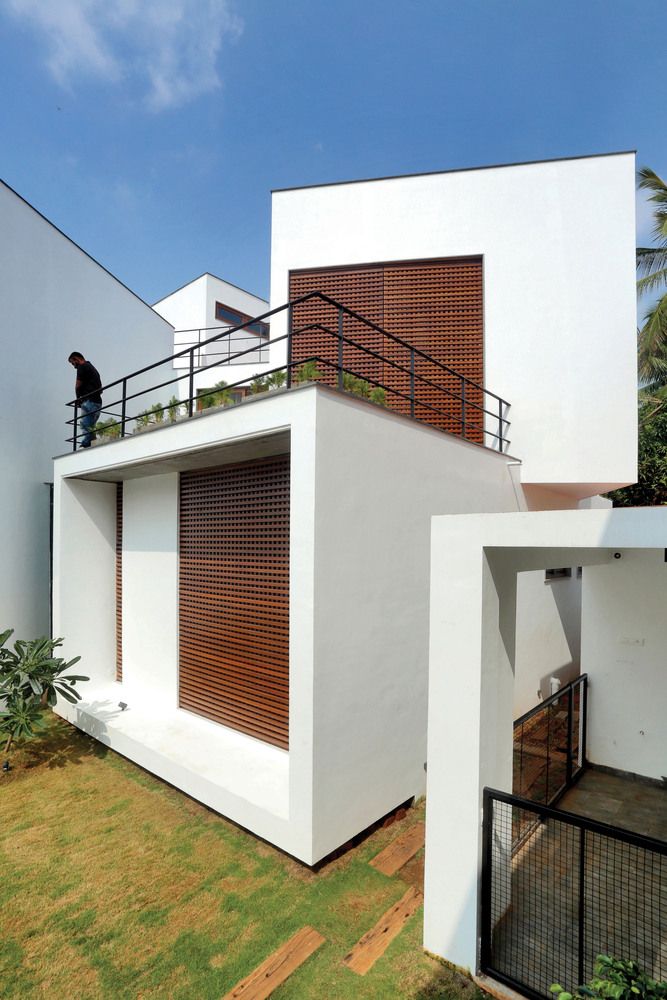 a man standing on top of a balcony next to a white building with wooden shutters