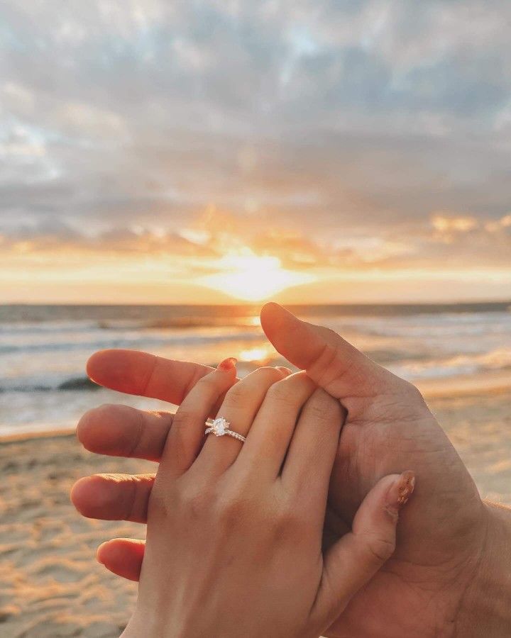 two people holding each other's hand on the beach at sunset with the sun setting in the background