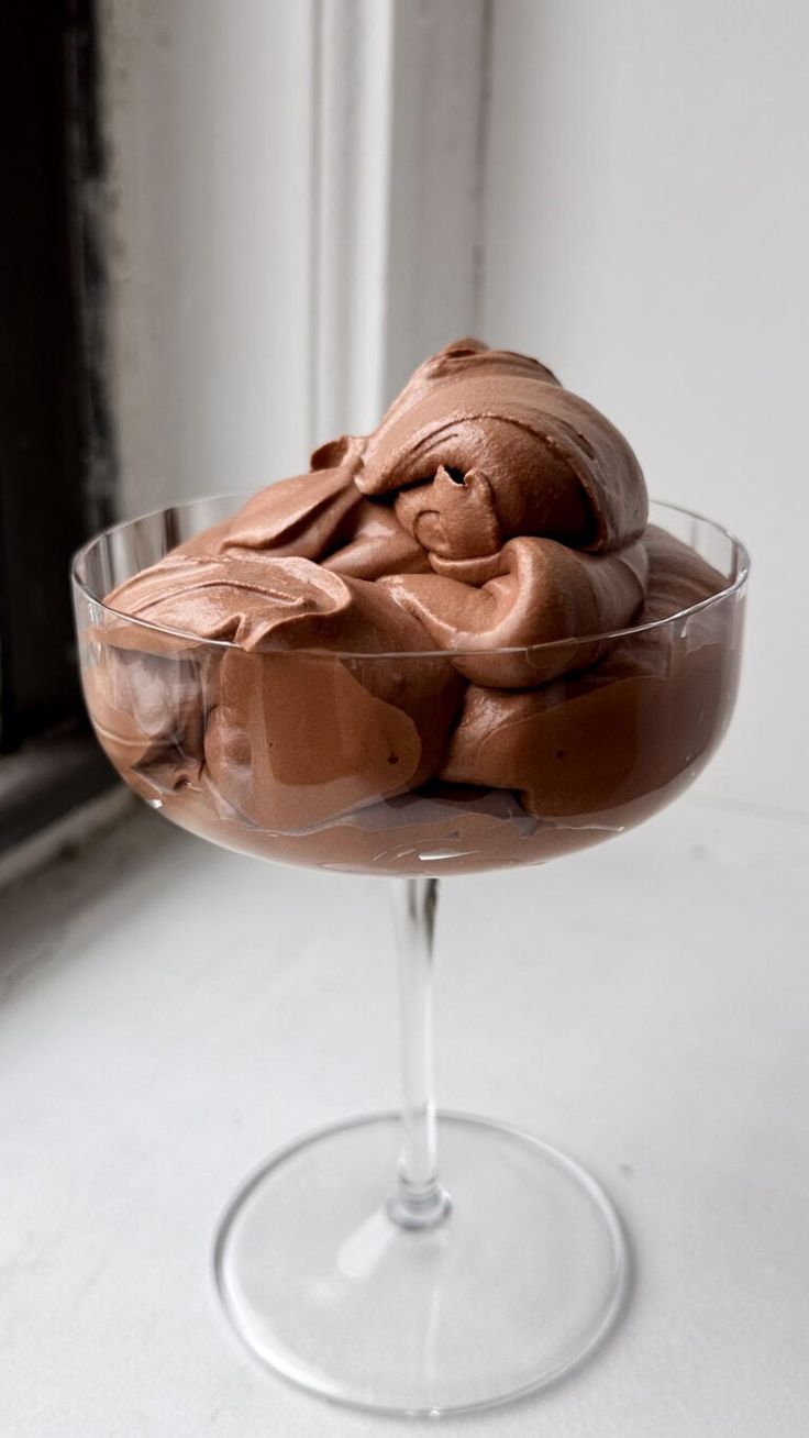 a glass bowl filled with chocolate dessert on top of a counter next to a window