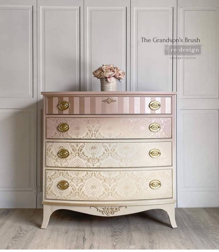 an antique dresser with pink and gold paint on the top, in front of white paneled walls