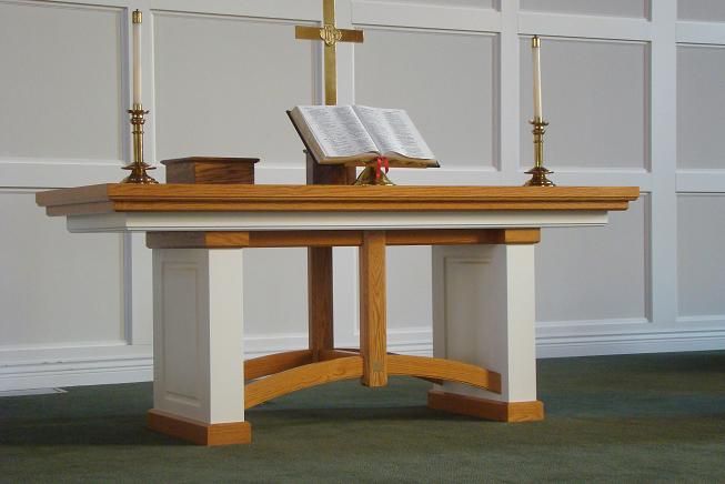 a wooden table with a book on top of it next to two candles and a cross