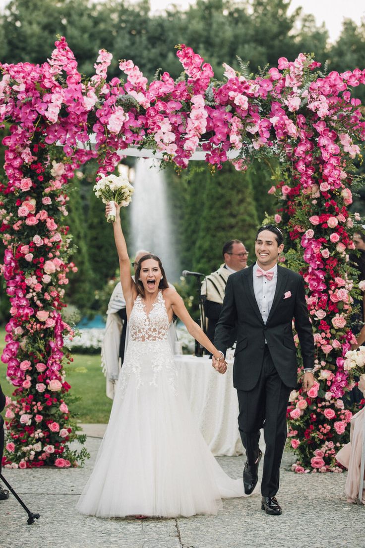 a bride and groom holding hands in front of a floral arch