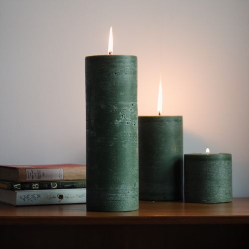 three green candles sitting on top of a wooden table next to books and a lamp