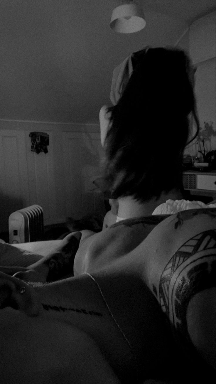 a woman laying in bed with tattoos on her back