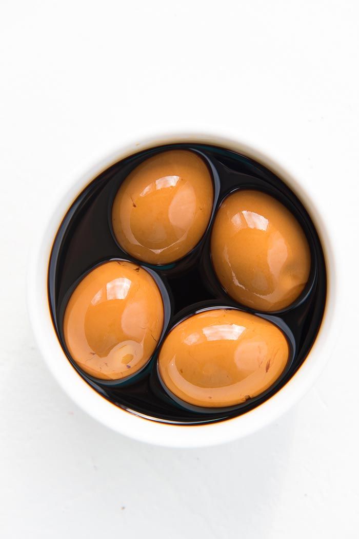 four brown eggs in a black and white bowl on a white table top with water