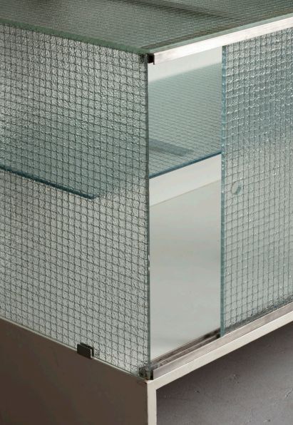 a metal and glass cabinet with two shelves on each side, in front of a gray wall