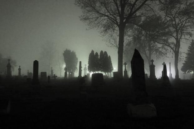 foggy graveyard at night with headstones lit up in the distance and trees on either side