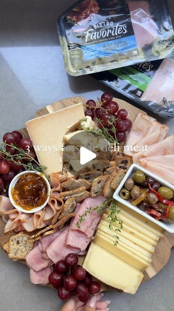 an assortment of cheeses, meats and grapes on a wooden platter with crackers