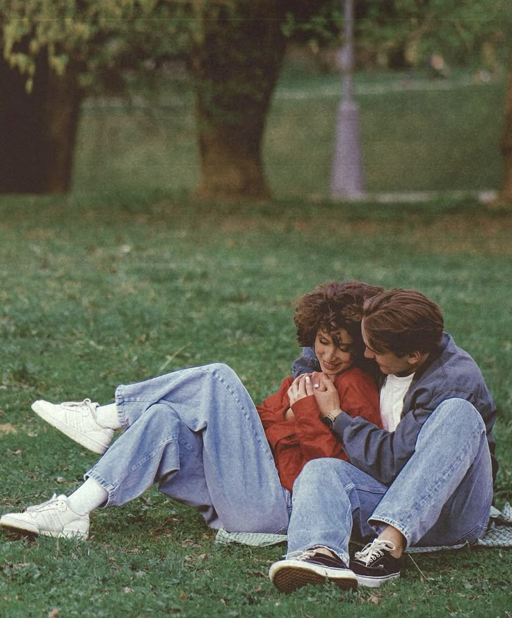 two people sitting on the grass with their arms around each other