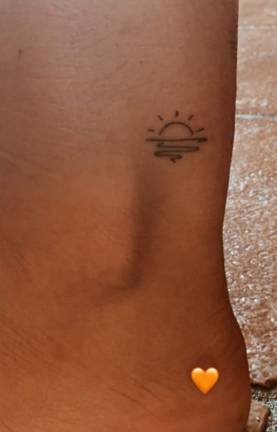 a small sun tattoo on the side of a woman's leg with an orange heart