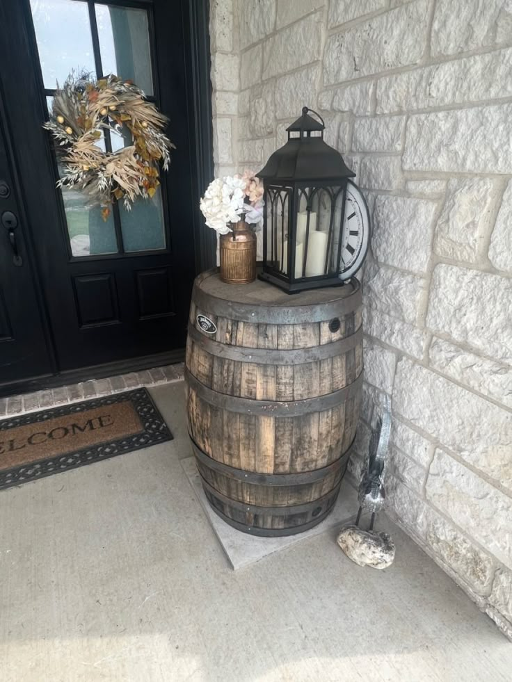 a wooden barrel sitting next to a door with a lantern on it and flowers in the vase