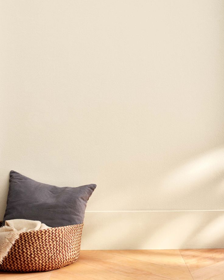 a pillow on the floor in front of a white wall with a basket underneath it