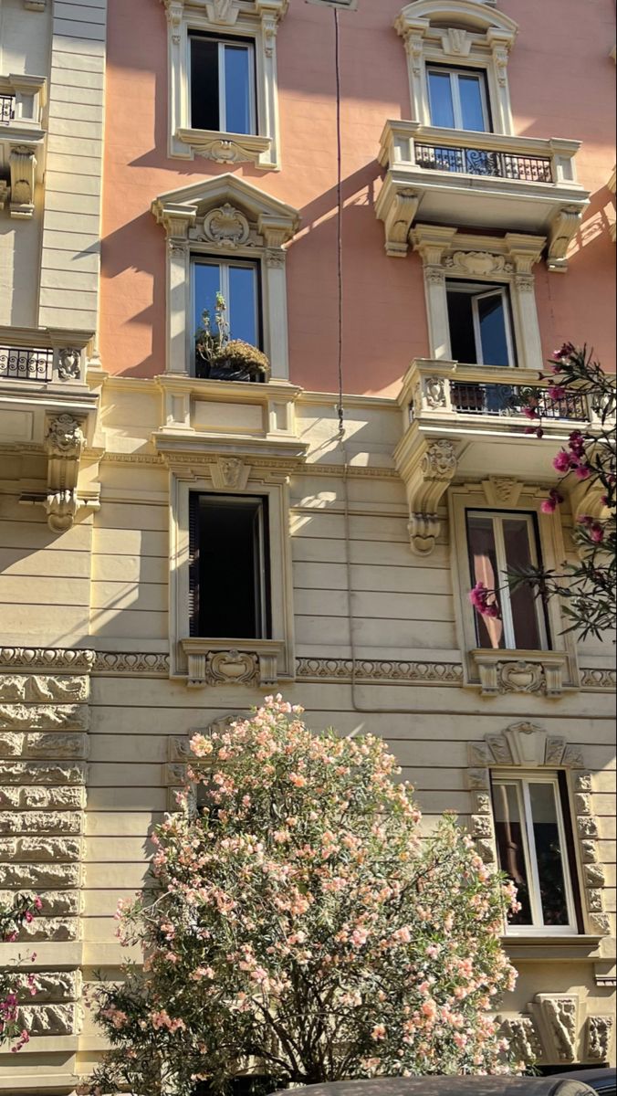 an apartment building with many windows and balconies on the second floor, next to a tree