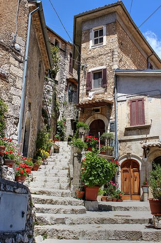 an old stone building with potted plants and flowers on the steps leading up to it