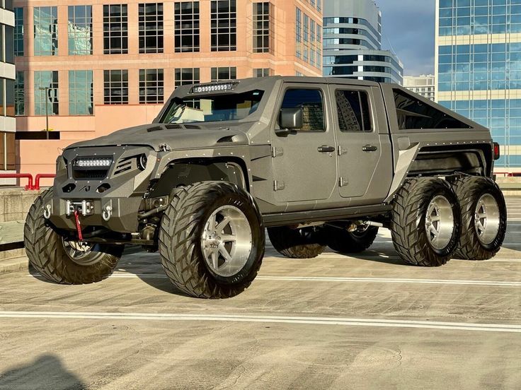 a large gray truck parked on top of a parking lot in front of tall buildings