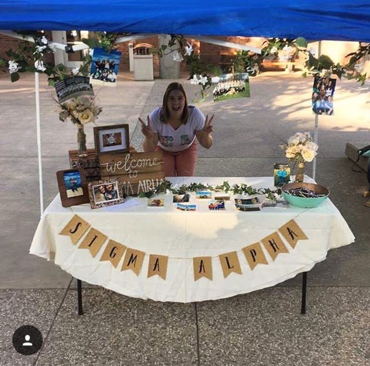 a woman standing behind a table that has some pictures on it and signs in front of it