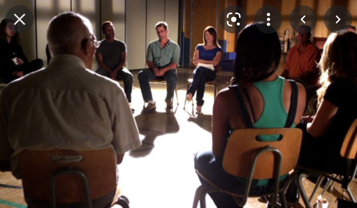 a group of people sitting in chairs talking to each other and one person standing up