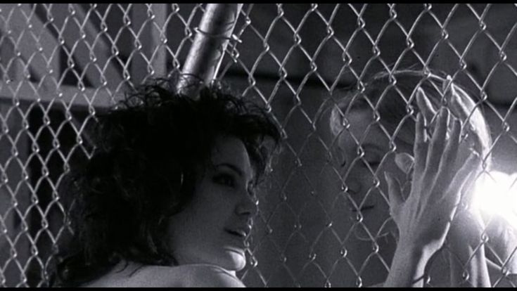 two women standing next to each other in front of a chain link fence with light shining through them