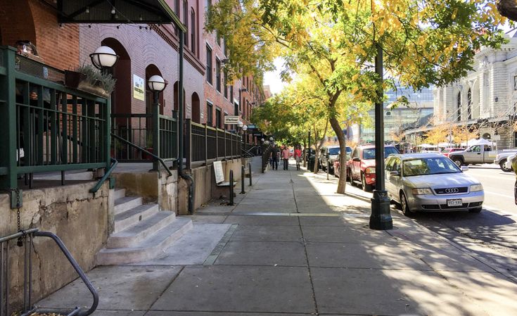 a city street lined with parked cars next to tall brick buildings and green railings