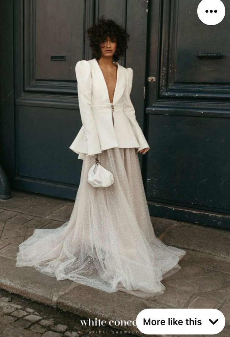 a woman standing in front of a black door wearing a white dress and blazer