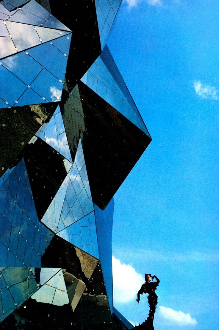 a man standing on top of a rock next to a tall building with mirrored windows