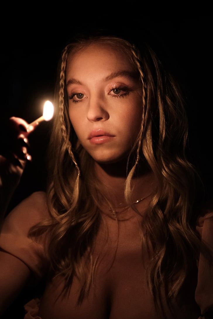 a young woman holding a lit candle in her right hand and looking at the camera