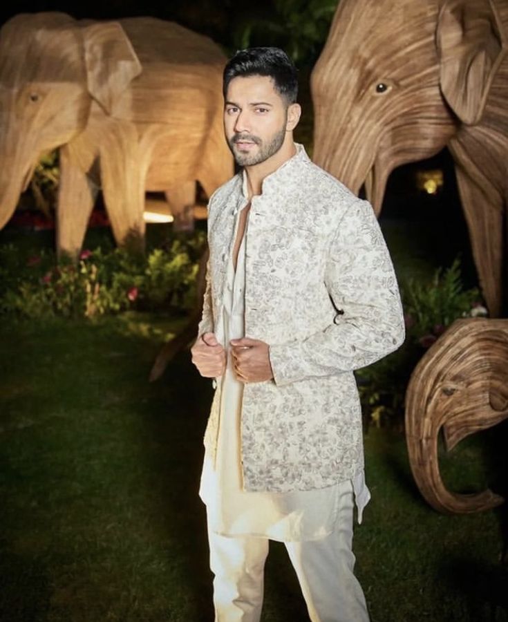 a man standing in front of an elephant statue with his hand on his hip and wearing a white suit