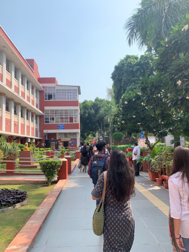 people are walking down the sidewalk in front of a building with many plants and trees