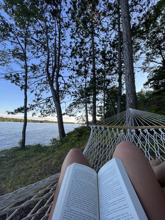 a person reading a book in a hammock by the water with trees on both sides