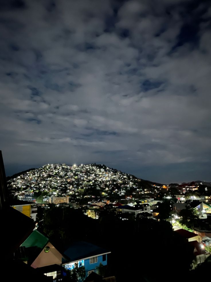 the city lights shine brightly in the night sky over houses and hills on a hill