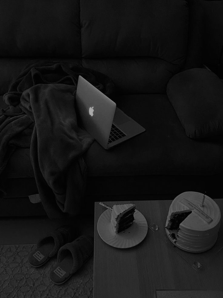 an open laptop computer sitting on top of a table next to a piece of cake