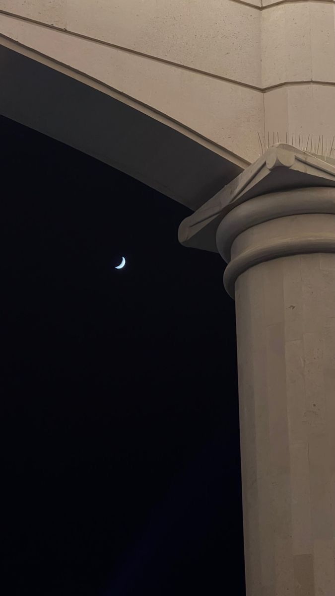 the moon is visible in the sky over an arch on a building's roof