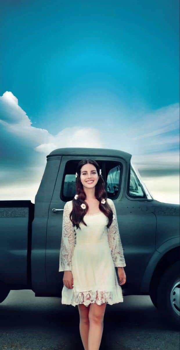 a woman standing in front of a pick up truck with clouds and blue sky behind her