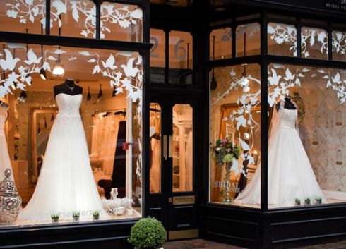 wedding dresses are displayed in the window of a storefront at night, as well as flowers and vases