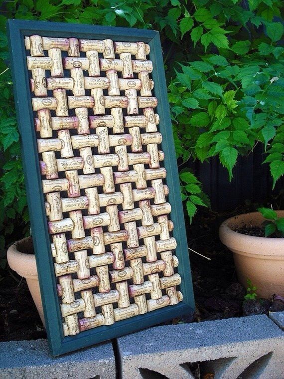 a framed cork art piece sitting on top of a cement block next to potted plants