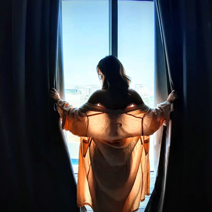 a woman standing in front of a window with her back turned to the camera and wearing sheer clothing