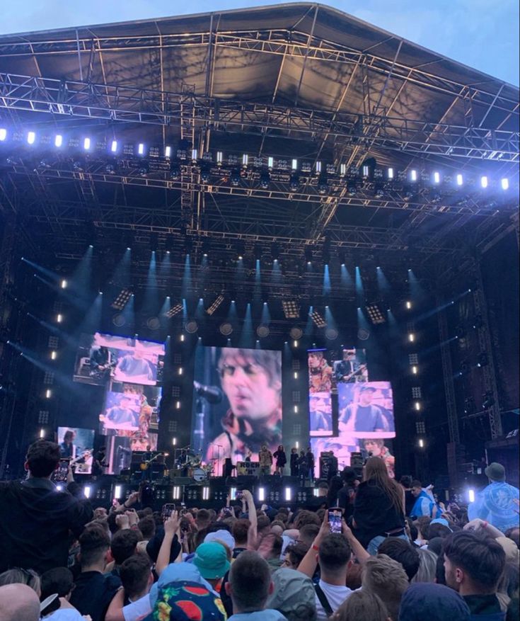 a large crowd at a concert with people taking pictures on their cell phones and the stage is lit up