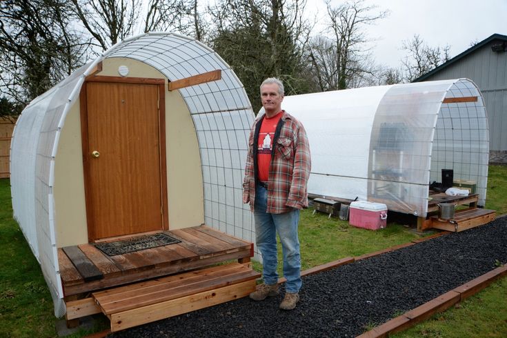 a man standing in front of a small house made out of wood and plastic sheeting