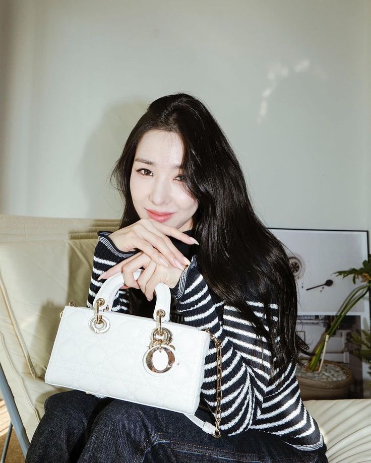 a woman sitting on top of a couch holding a white handbag in her right hand