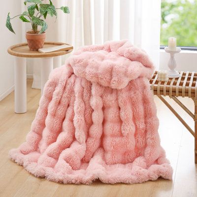 a pink blanket sitting on top of a wooden floor next to a table and chair