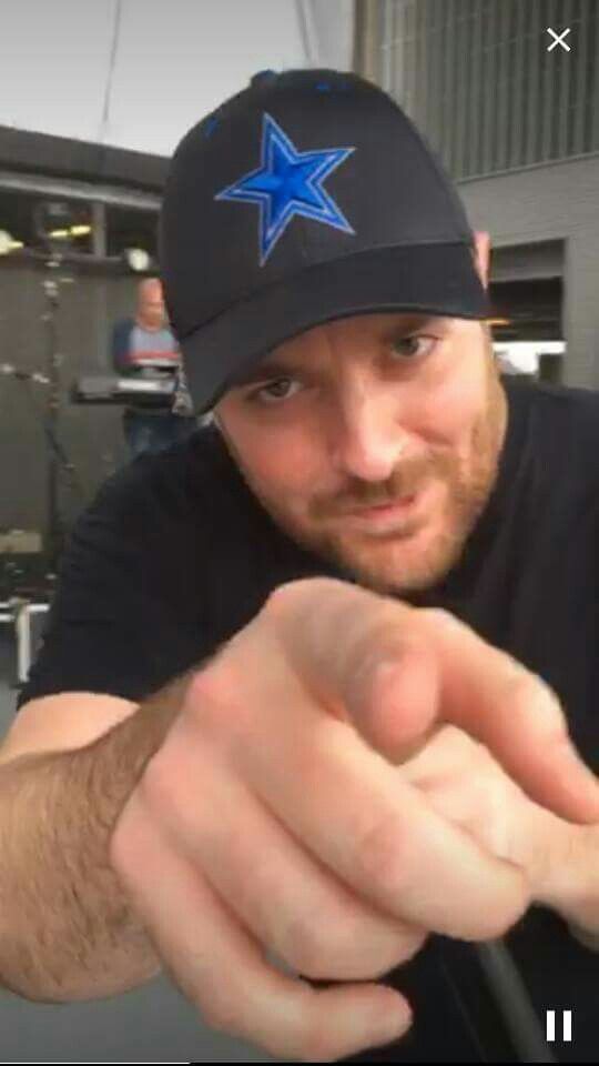 a man pointing at the camera while wearing a black hat with a blue star on it