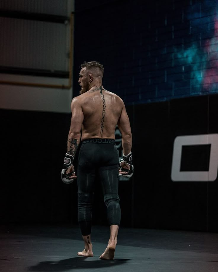 a man with no shirt is walking on the stage wearing gloves and holding two hands behind his back