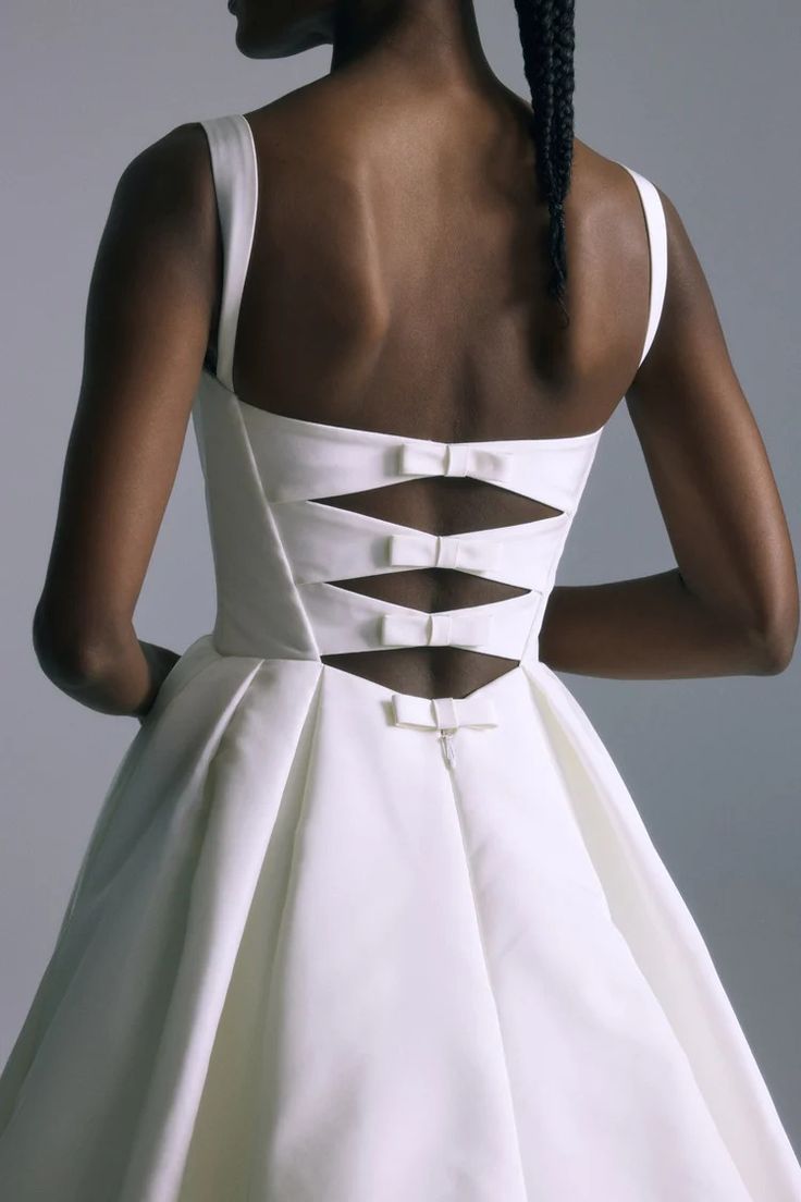 the back of a woman's white dress with cutouts on it and braids in her hair